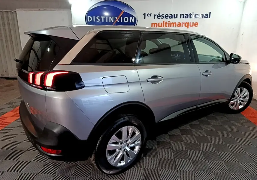 Peugeot 5008 gris clair vue 3/4 arrière droit, feux arrière LED allumés, intérieur visible à travers les vitres teintées.