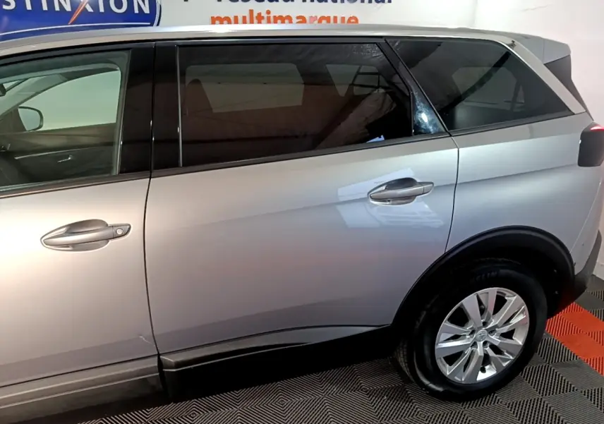Vue latérale côté droit d’un Peugeot 5008 gris clair, mettant en valeur les portes arrière et la roue arrière dans un intérieur showroom.