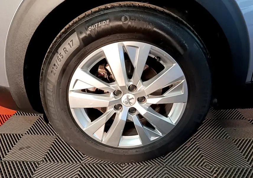 Gros plan sur la roue avant droite d’un Peugeot 5008 gris clair, avec jante alliage à cinq doubles branches.