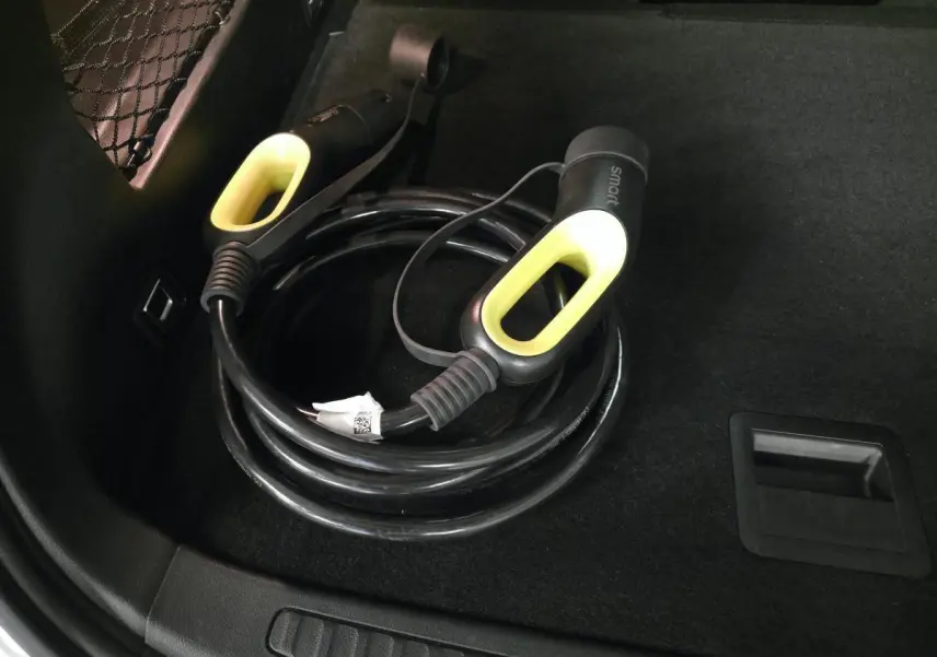 Gros plan sur le câble de recharge électrique noir avec poignées jaunes dans le coffre d'une Smart #1 blanche.
