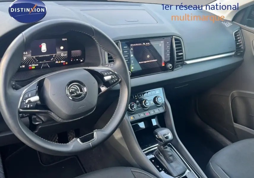 Vue intérieure du tableau de bord et volant du Skoda Karoq noir, avec écran tactile et commandes de climatisation visibles.