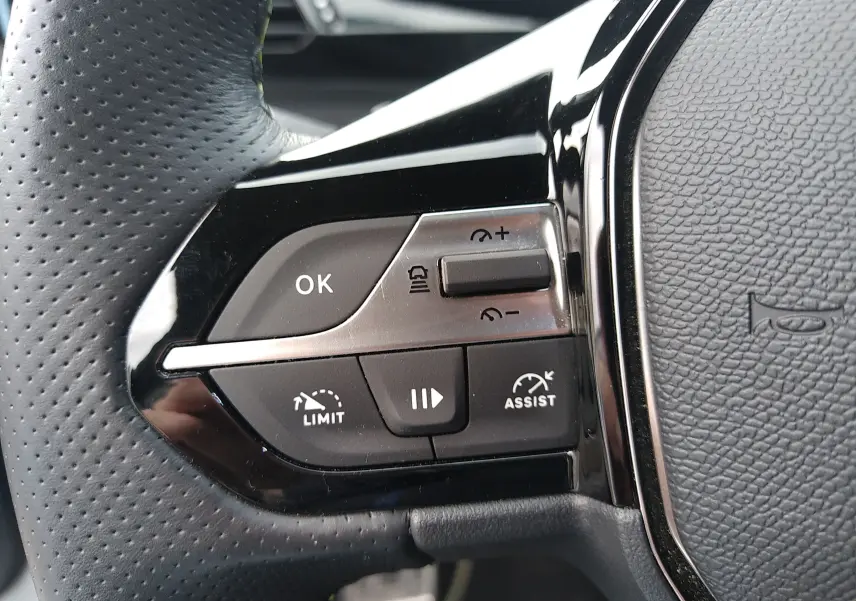 Gros plan sur les commandes gauche du volant en cuir perforé de la Peugeot 408 Hybrid blanc Okenite, avec boutons de limitation et assistance.