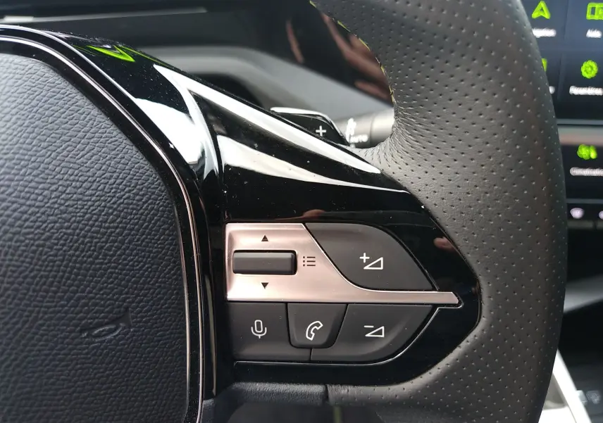 Gros plan sur les commandes multifonctions en plastique noir et argent du volant perforé d’un Peugeot 408 Hybrid 2024.