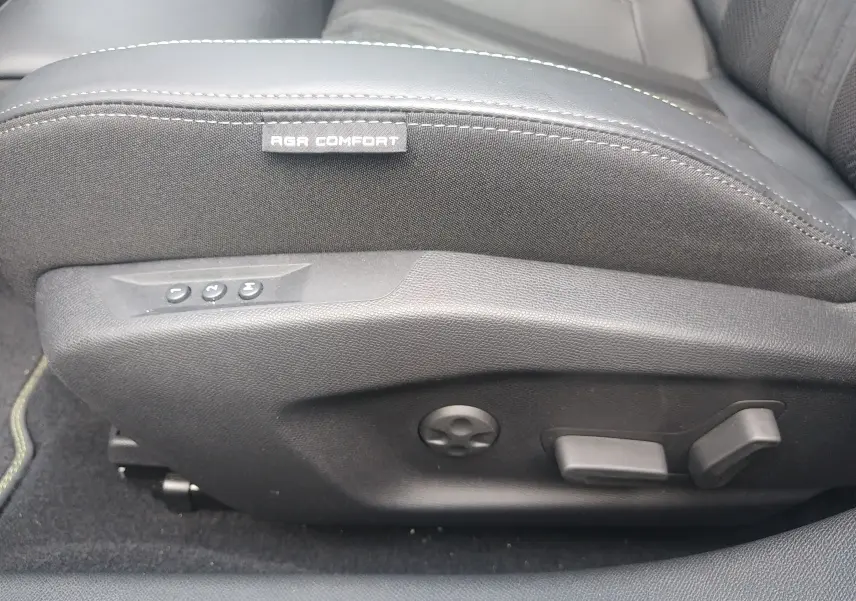 Détail du côté gauche du siège avant noir avec étiquette AGR Comfort et commandes de réglage électrique dans une Peugeot 408 Hybrid 2024.