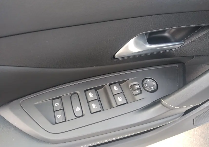 Gros plan sur la commande des vitres et rétroviseurs côté conducteur d’une Peugeot 408 blanche, intérieur noir.