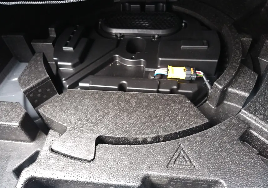 Détail du rangement sous le coffre de la Peugeot 408 Hybrid blanc Okenite, montrant le compartiment technique et câblage.