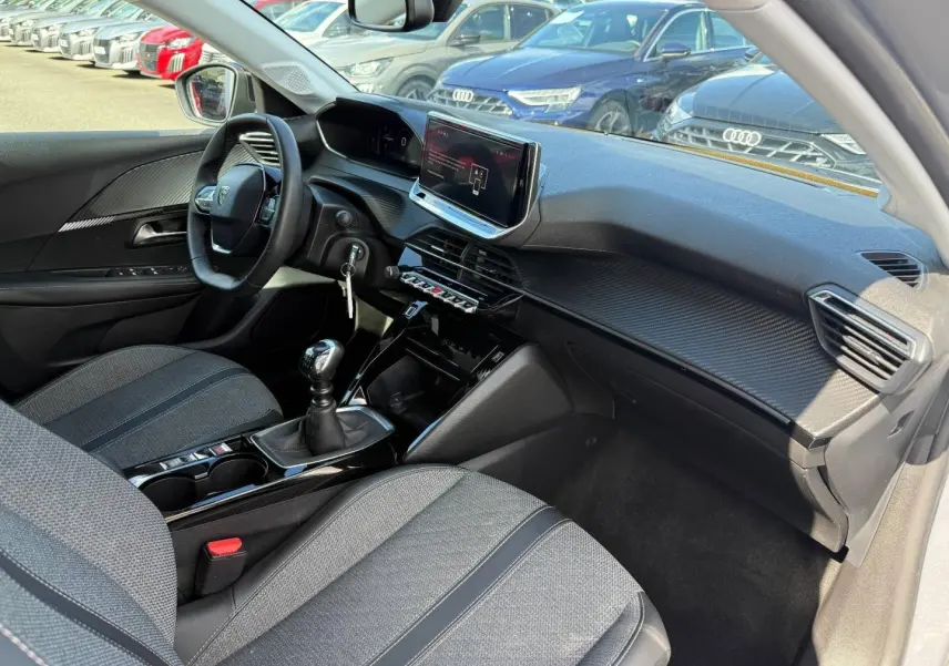 Vue intérieure côté passager de la Peugeot 208 2025 avec sellerie tissu gris et tableau de bord moderne noir.