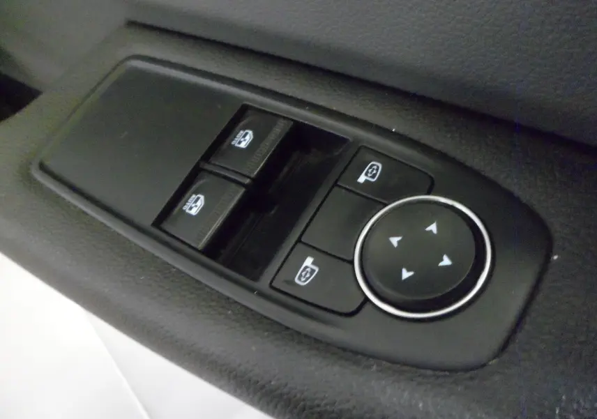 Gros plan sur les commandes électriques des vitres et des rétroviseurs côté conducteur d'une Renault Clio V blanche.