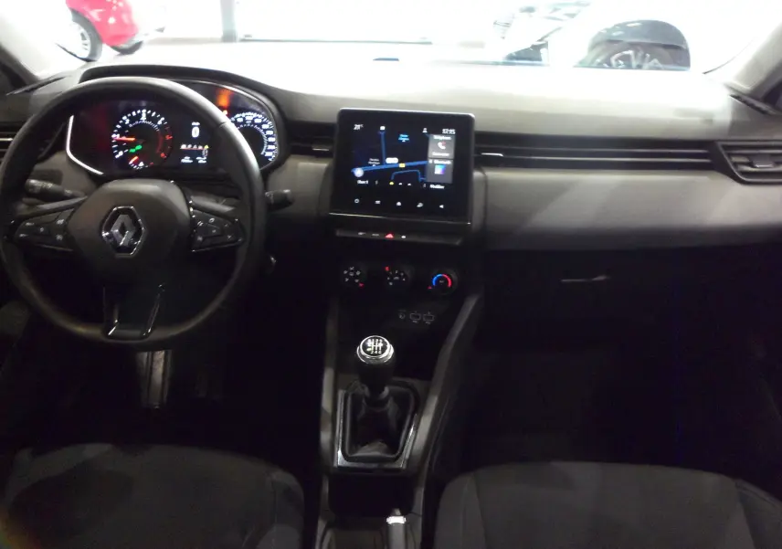 Vue intérieure centrée sur le tableau de bord et la console centrale d'une Renault Clio V blanche avec boîte manuelle.