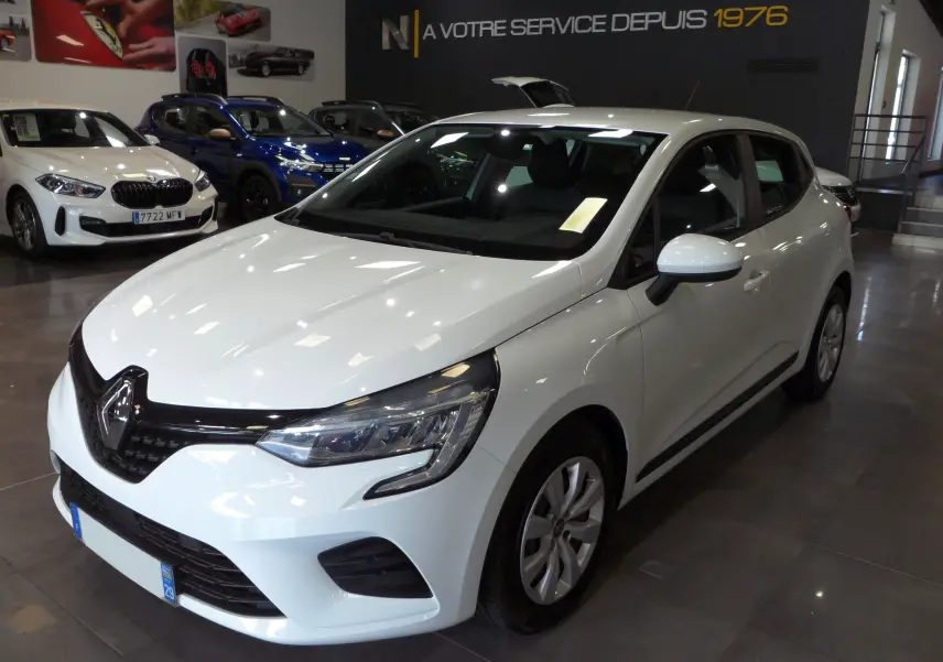Renault Clio V blanche Glacier vue 3/4 avant droit en showroom, avec phares modernes et calandre noire brillante.