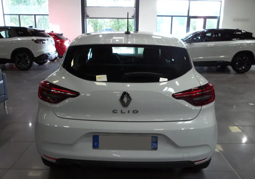 Vue arrière d'une Renault Clio V blanche Glacier en showroom, mettant en valeur ses feux arrière et son logo distinctif.