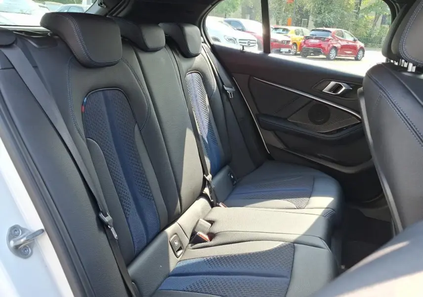 Vue intérieure sur les sièges arrière en cuir noir de la BMW Série 1 blanche, avec détails sport et habillage de porte visible.