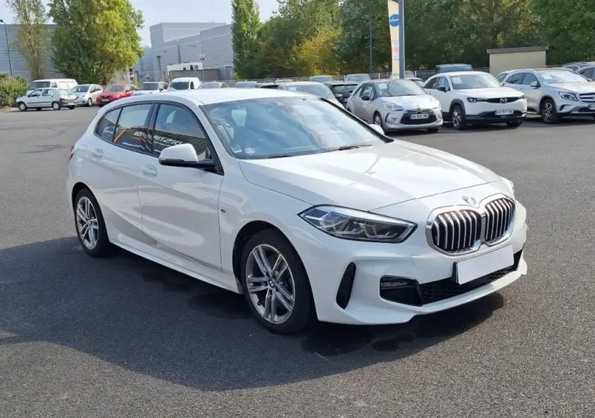 BMW Série 1 blanche vue en 3/4 avant droit, avec jantes alliage et calandre caractéristique M Sport.