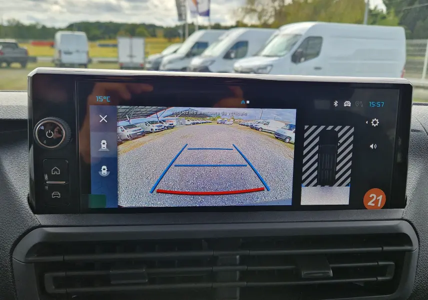 Écran central affichant la caméra de recul avec vue arrière sur un parking de véhicules utilitaires blancs.