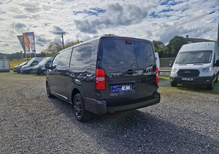 Vue 3/4 arrière d'un Citroën Jumpy XL gris titane avec vitres arrière teintées et jantes tôles 17 pouces sur parking extérieur.