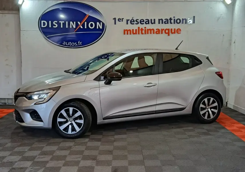 Profil droit d'une Renault Clio 2023 gris clair, avec jantes bicolores et rétroviseurs noirs, en intérieur showroom.