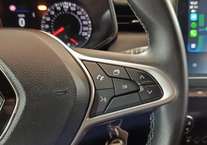 Gros plan sur les commandes multifonctions à droite du volant cuir noir de la Renault Clio gris clair 2023, avec tableau de bord partiellement visible.