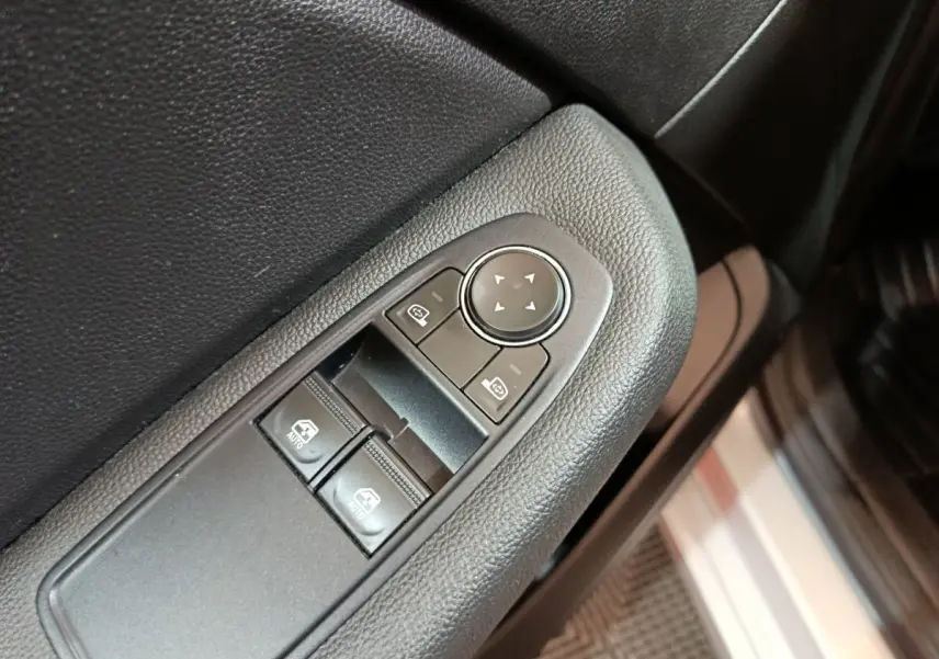 Gros plan sur les commandes de lève-vitres et rétroviseurs côté conducteur d’une Renault Clio gris clair 2023.