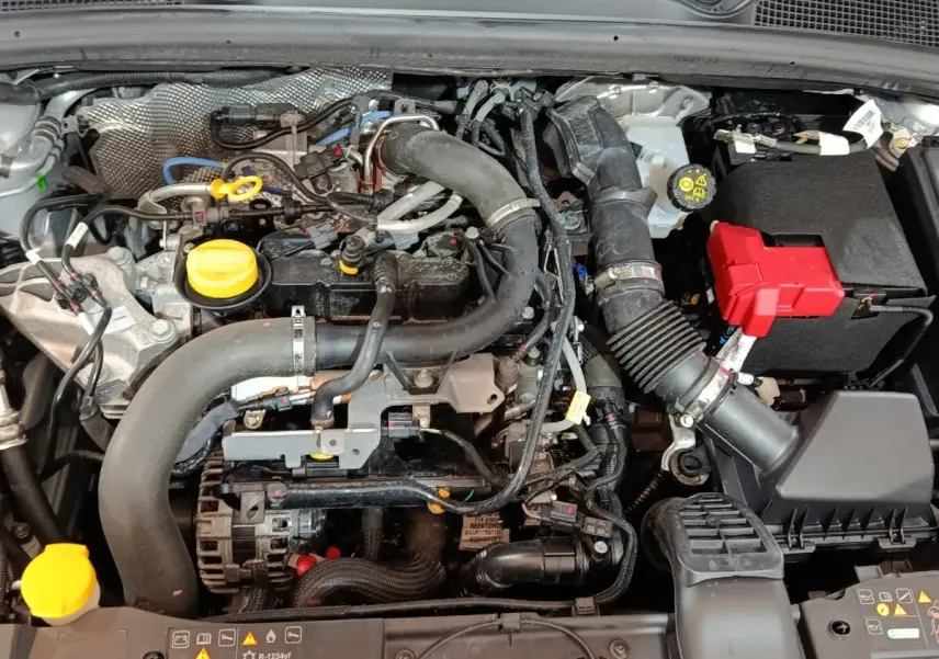 Gros plan sur le moteur essence d'une Renault Clio 2023, avec bouchons jaunes et batterie à capot rouge visible.