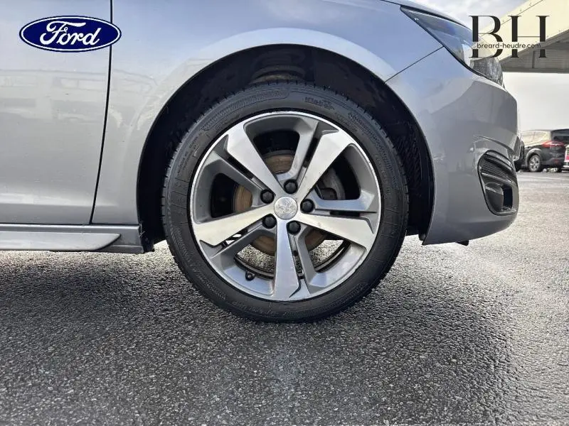 Gros plan sur la roue avant droite d'une Peugeot 308 SW gris Artense, avec jante alliage et logo Peugeot central.