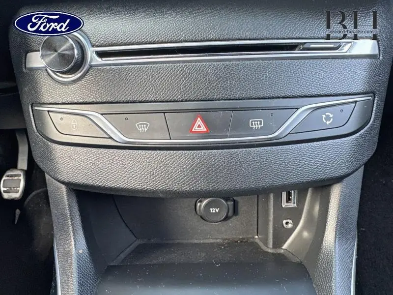 Vue rapprochée du tableau de bord noir avec commandes centrales et prise 12V d'une Peugeot 308 SW gris Artense.