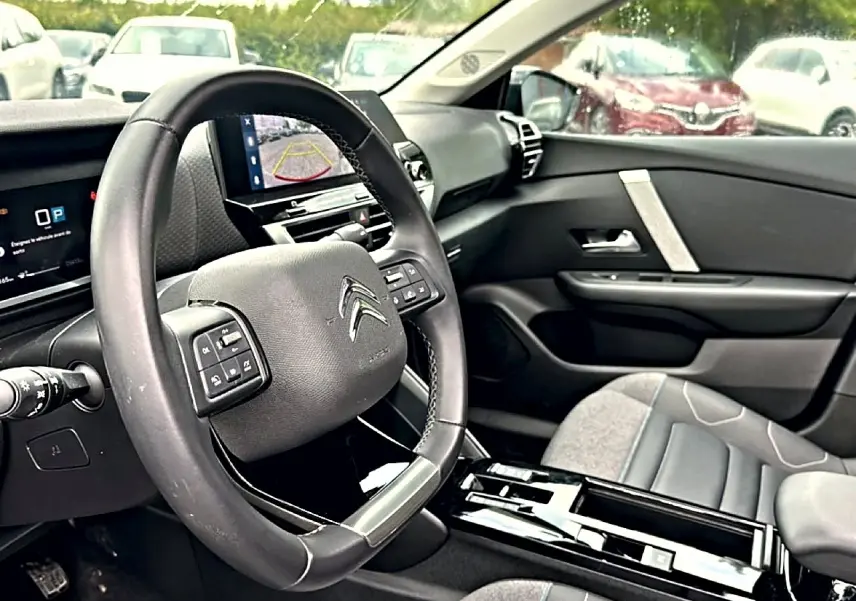 Vue intérieure côté conducteur de la Citroën C4 2024, volant cuir noir et écran tactile affichant la caméra de recul.