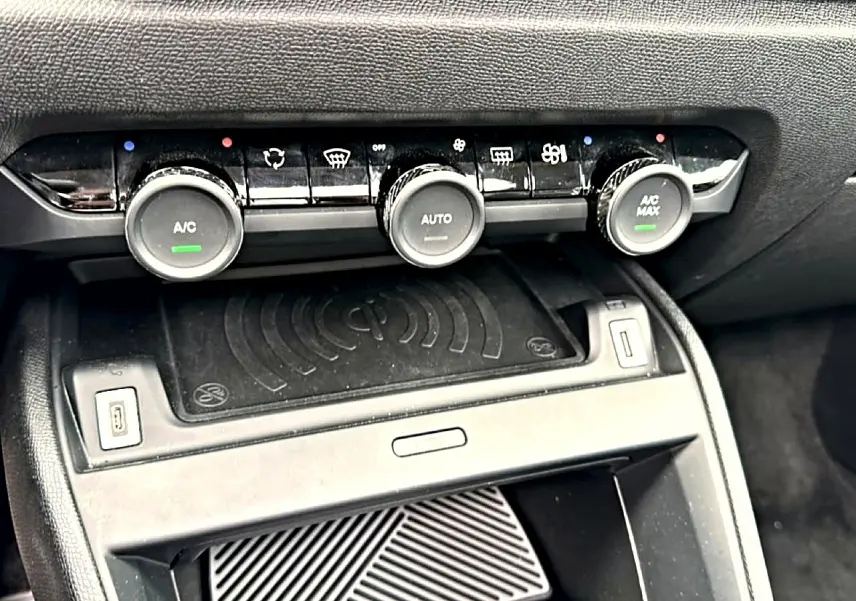 Détail de la console centrale noire avec commandes climatisation automatique et zone de charge sans fil dans une Citroën C4 gris 2024.