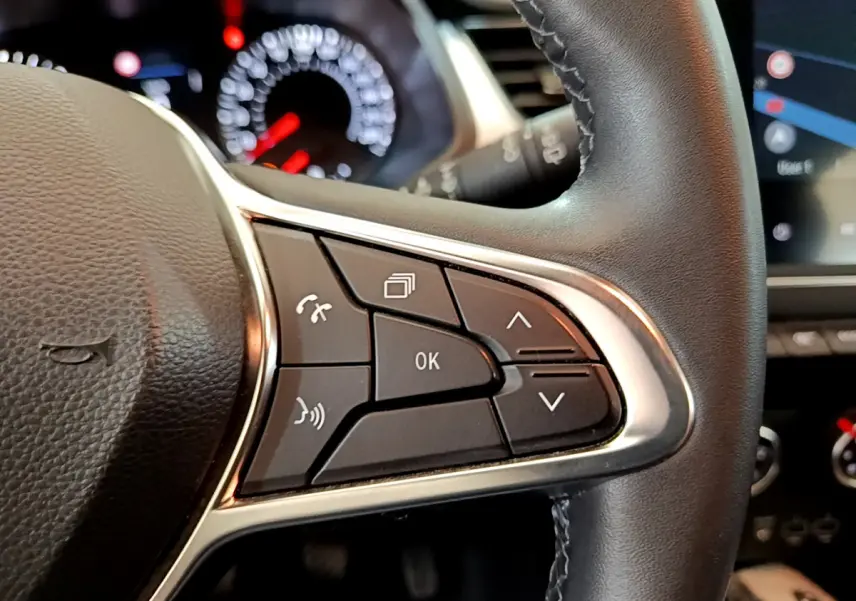 Gros plan sur les commandes multifonctions du volant côté droit du Renault Captur noir, tableau de bord flou en arrière-plan.