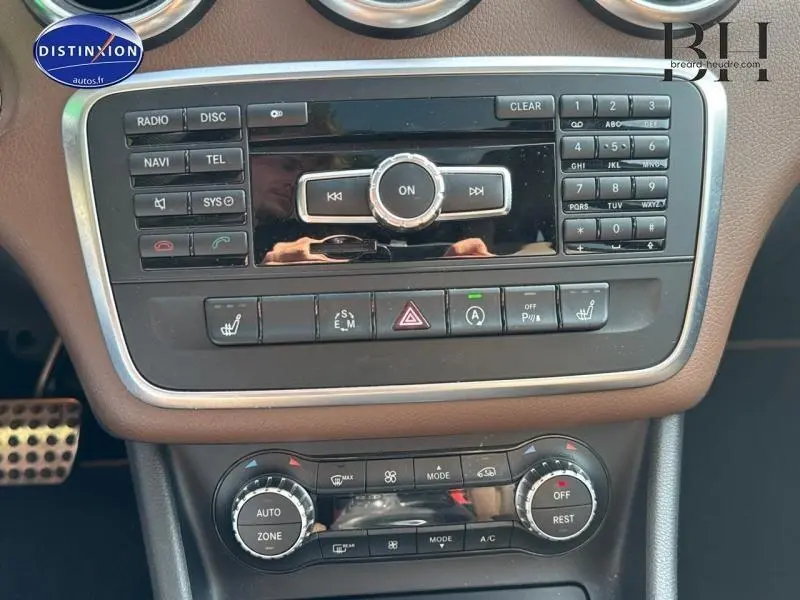 Vue rapprochée de la console centrale marron avec commandes radio, climatisation et boutons multifonctions d'une Mercedes Classe A gris Montagne.