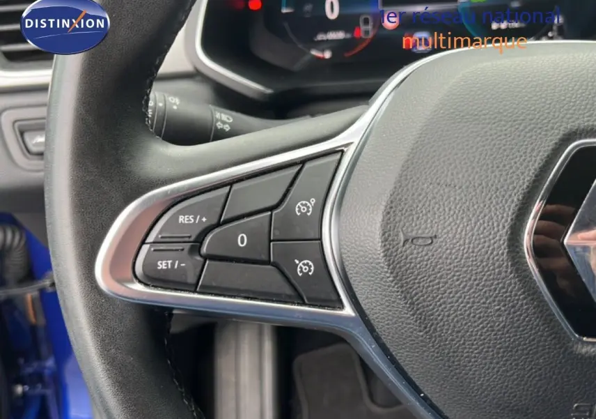 Gros plan sur le volant noir du Renault Captur bleu Iron Metal, avec commandes intégrées et logo Renault visible.