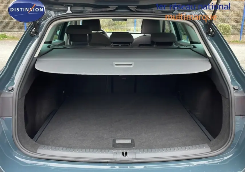 Coffre ouvert vu de l'arrière d'une SEAT LEON ST 2025 bleu Fjord, avec cache-bagages déployé et espace de chargement vide.