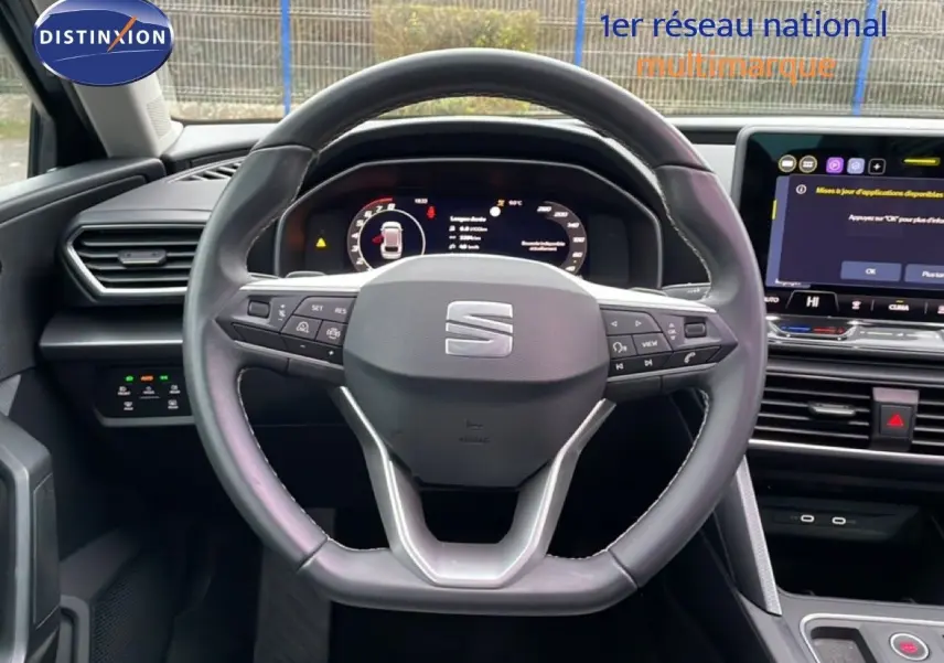 Vue intérieure centrée sur le volant cuir multifonction de la SEAT LEON ST IV 2025 avec tableau de bord numérique et écran tactile.