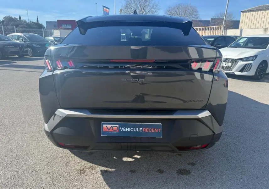Vue arrière d’un Peugeot 3008 Hybrid gris 2025 avec feux arrière à griffes et logo Peugeot lumineux.
