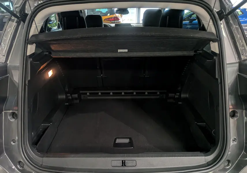 Coffre ouvert vu de l'arrière d'un Citroën C5 Aircross gris Platinium avec cache-bagages relevé et intérieur noir.