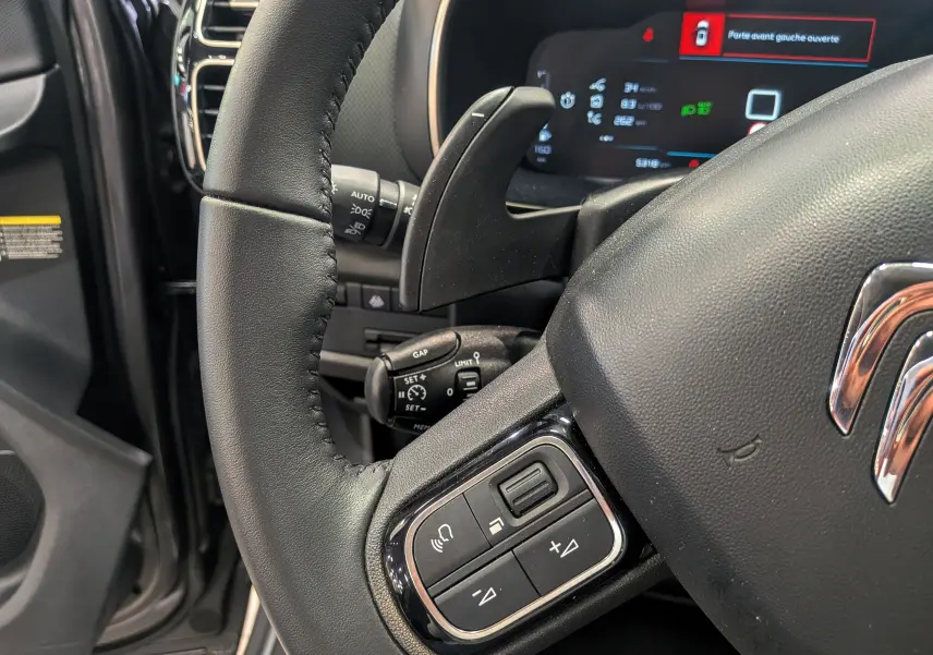 Gros plan sur le volant cuir noir du Citroën C5 Aircross hybride 2025, avec commandes intégrées et tableau de bord numérique.