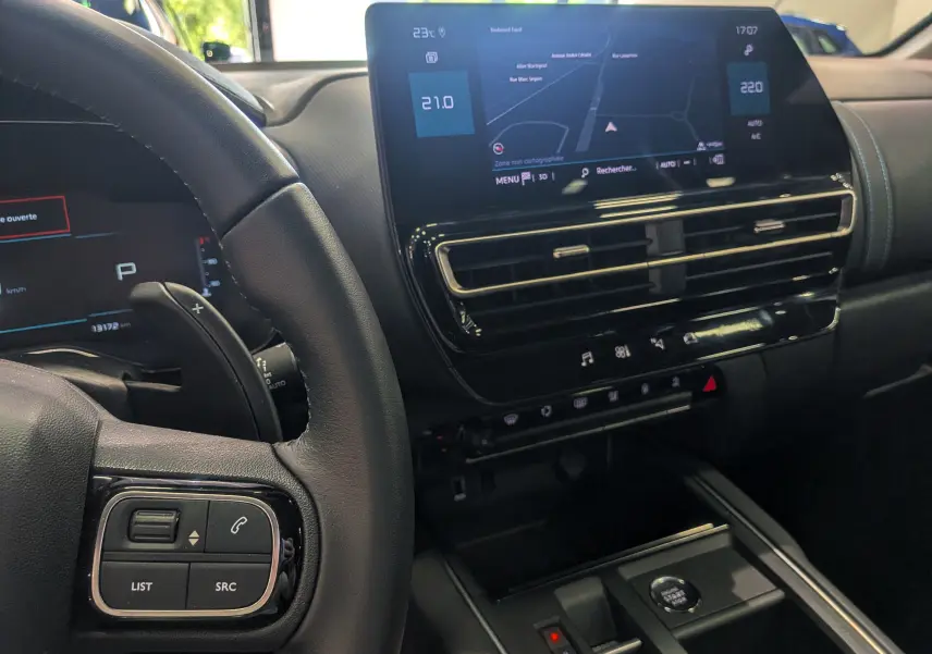 Vue intérieure centrée sur le tableau de bord et l'écran tactile du Citroën C5 Aircross hybride 2025, volant partiellement visible.