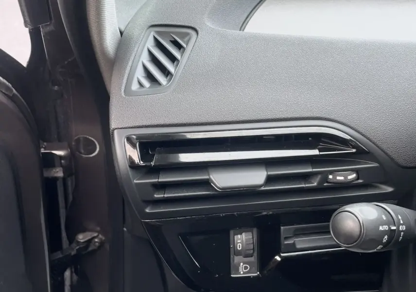 Détail de la console côté gauche d'une Citroën C4 Picasso marron, montrant les aérateurs et commandes d'éclairage.