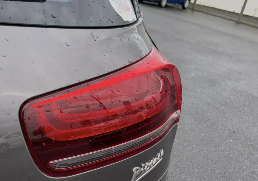 Gros plan sur le feu arrière droit d'une Citroën C4 Picasso marron sous la pluie, avec logo Picasso visible.