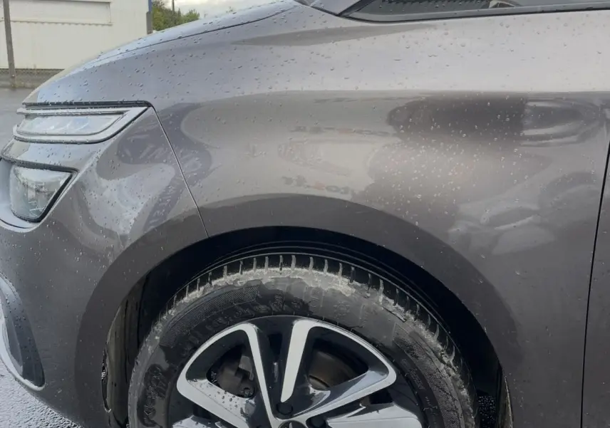 Gros plan sur la roue avant gauche et l'aile d'une Citroën C4 Picasso marron sous la pluie avec jante alu bicolore.