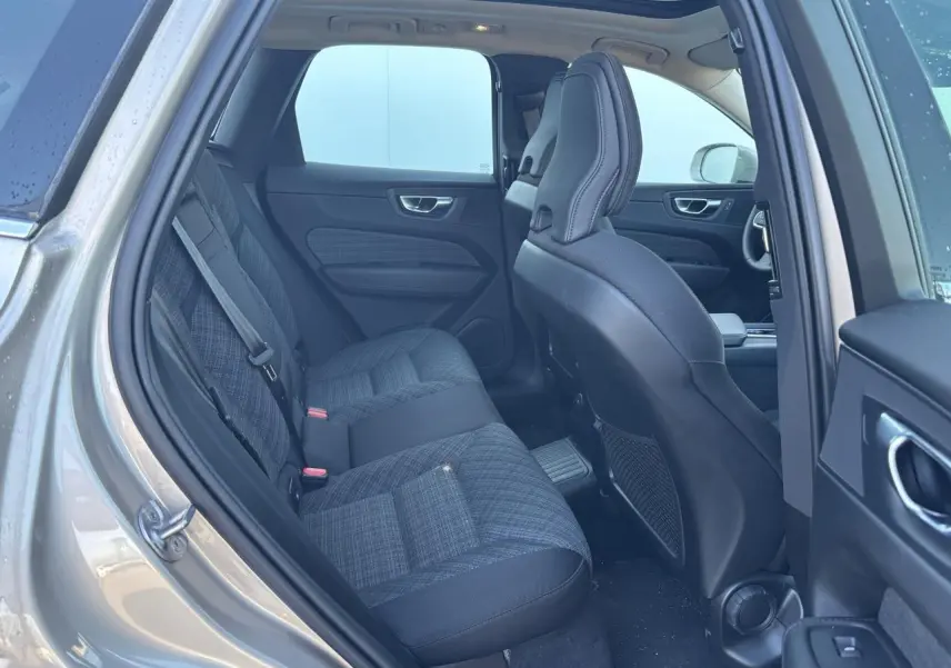 Vue intérieure côté gauche arrière du Volvo XC60 2024 argent crépuscule, sièges tissu gris à motifs et toit panoramique visible.