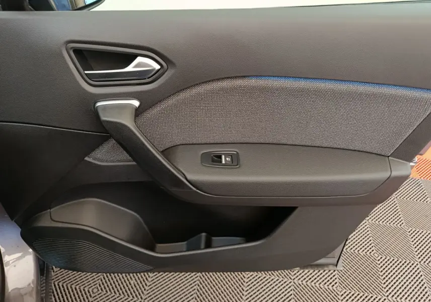 Gros plan sur la porte côté gauche du Renault Captur gris foncé, montrant la poignée et le bouton de lève-vitre.