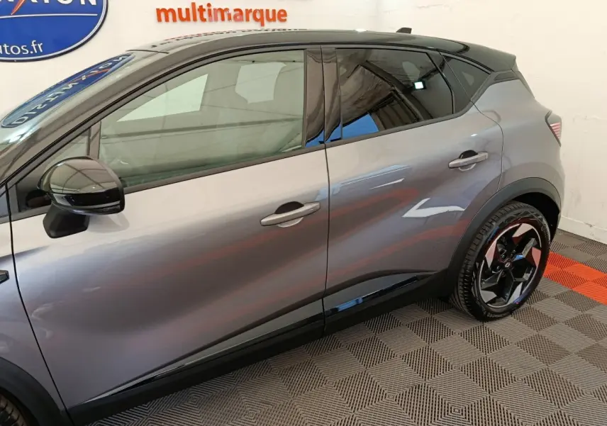 Profil côté gauche du Renault Captur gris foncé 2025 avec jantes noires et toit noir brillant visible en intérieur showroom