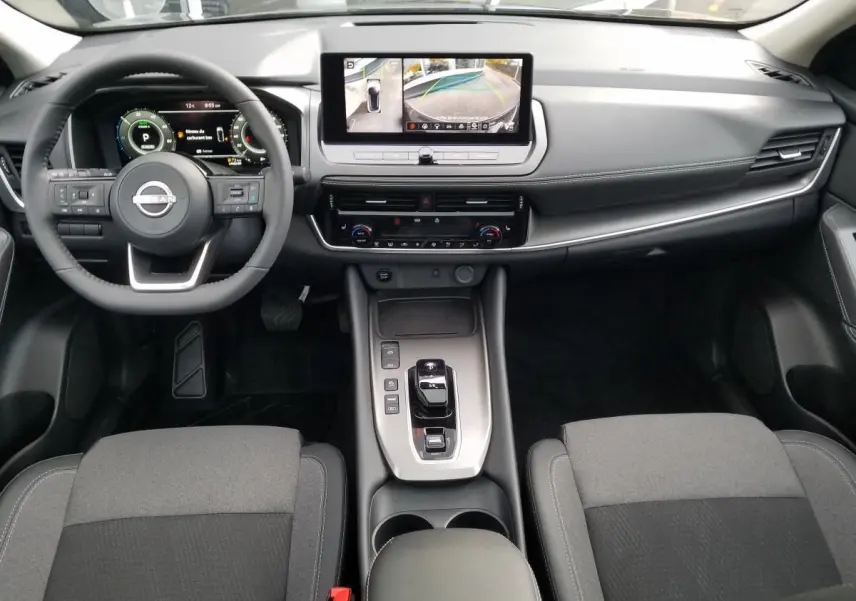 Vue intérieure avant du Nissan Qashqai 1.5 E-POWER 2025, tableau de bord noir avec écran central et volant multifonction.