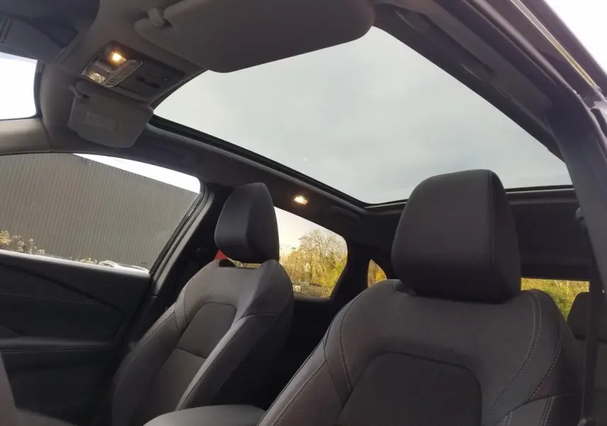 Vue intérieure avant du Nissan Qashqai noir 2025, mettant en valeur les sièges et le toit panoramique en verre.