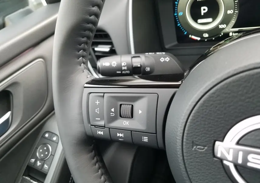 Gros plan sur le volant noir du Nissan Qashqai 2025 montrant les commandes multifonctions à gauche et le tableau de bord numérique.