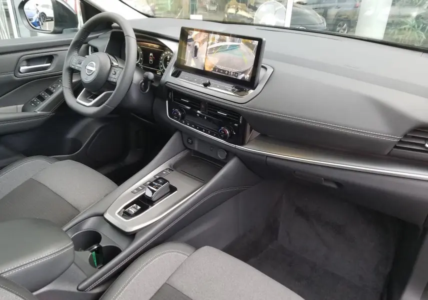 Vue intérieure avant droite du Nissan Qashqai 1.5 E-POWER 2025 avec écran tactile, volant multifonction et console moderne.