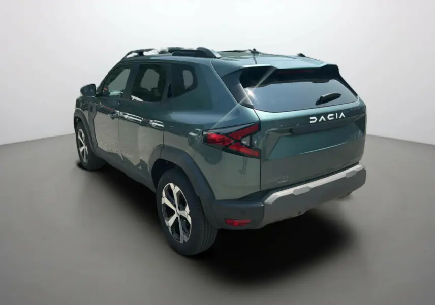 Vue 3/4 arrière droite du Dacia Duster 2025 vert cèdre avec jantes alu 18 pouces et barres de toit noires.