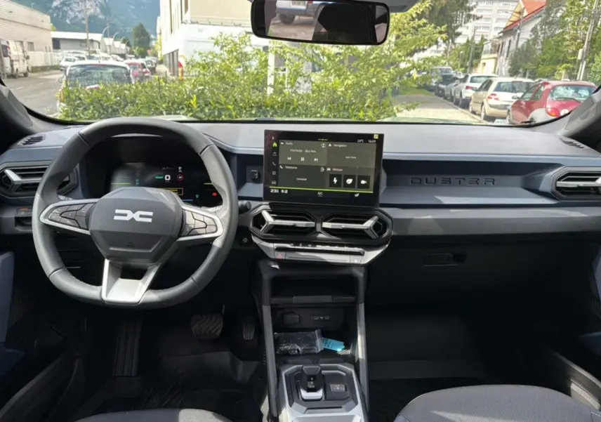 Vue intérieure frontale du tableau de bord du Dacia Duster 2025, avec écran tactile central et volant cuir noir.