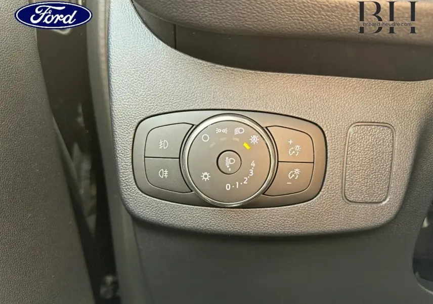 Gros plan sur le bouton de réglage des phares du Ford Puma 2023 en intérieur noir texturé.