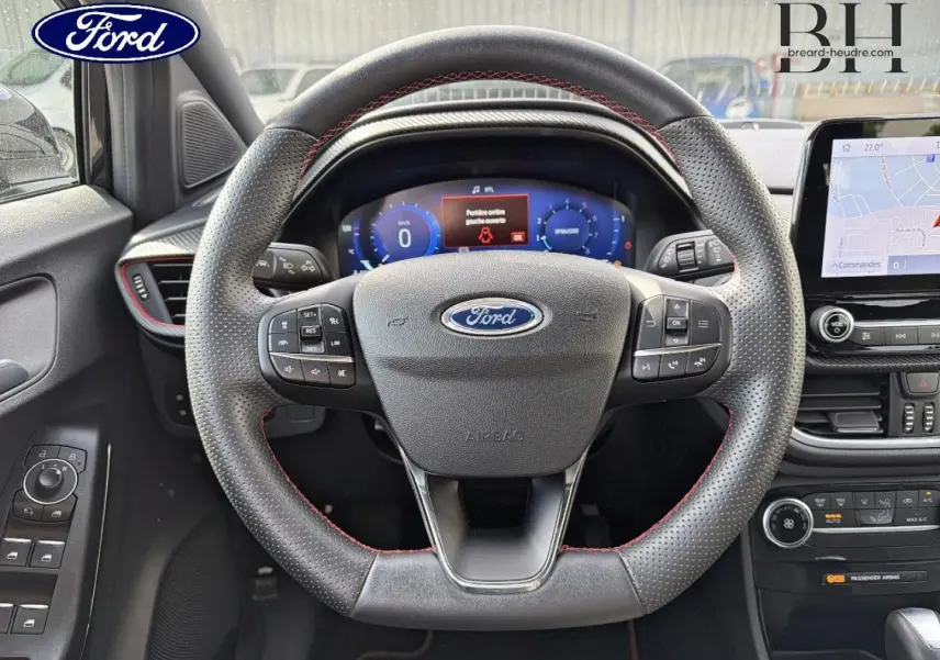 Vue intérieure centrée sur le volant perforé avec surpiqûres rouges du Ford Puma 2023, tableau de bord numérique et écran tactile visible.